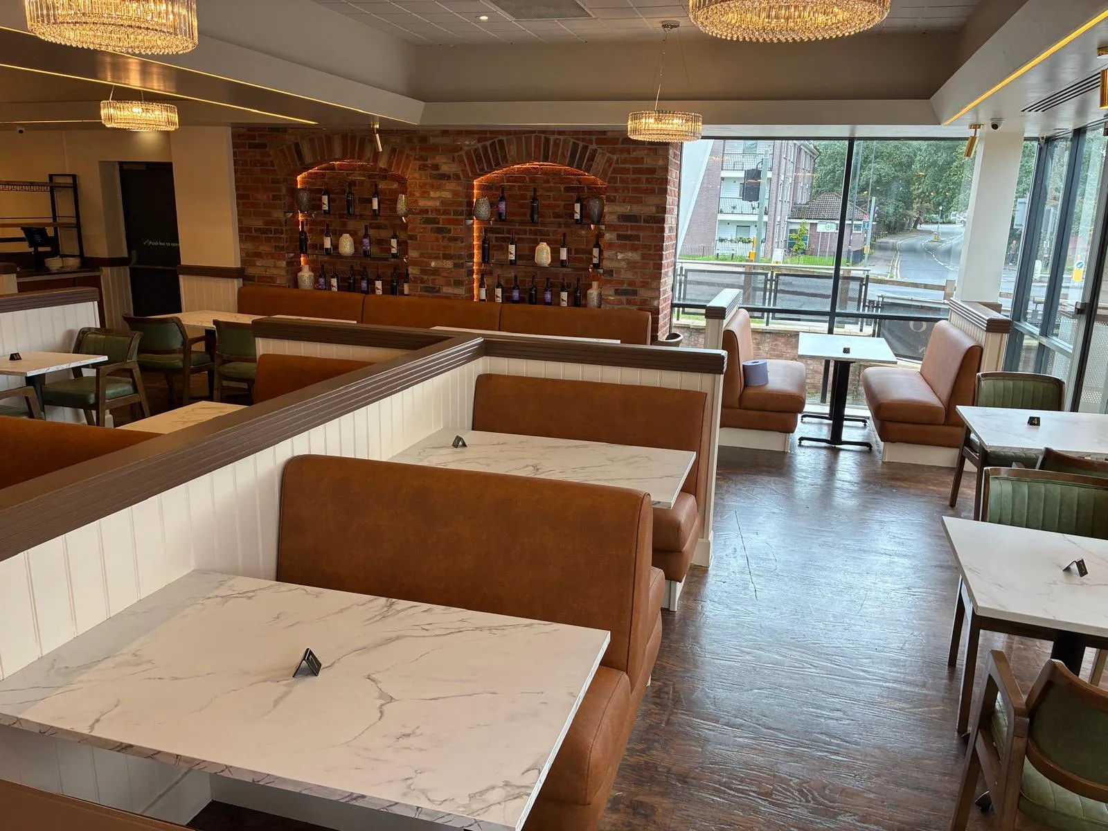 Restaurant in Altrincham with tan booths and wall banquettes, marble-effect tables and a brick wine wall