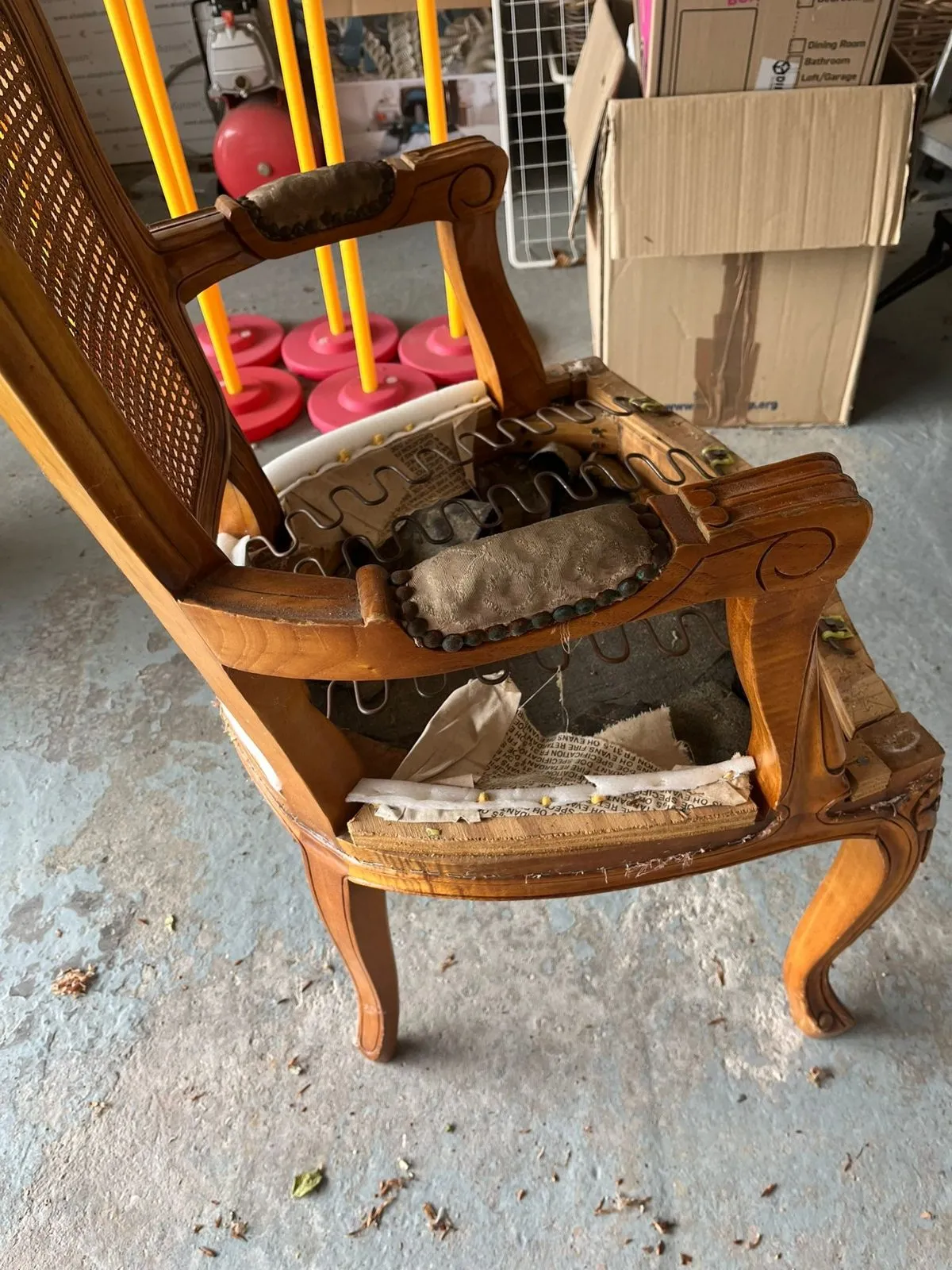 Carved cane-back armchair stripped back to its frame and springs on the workshop floor