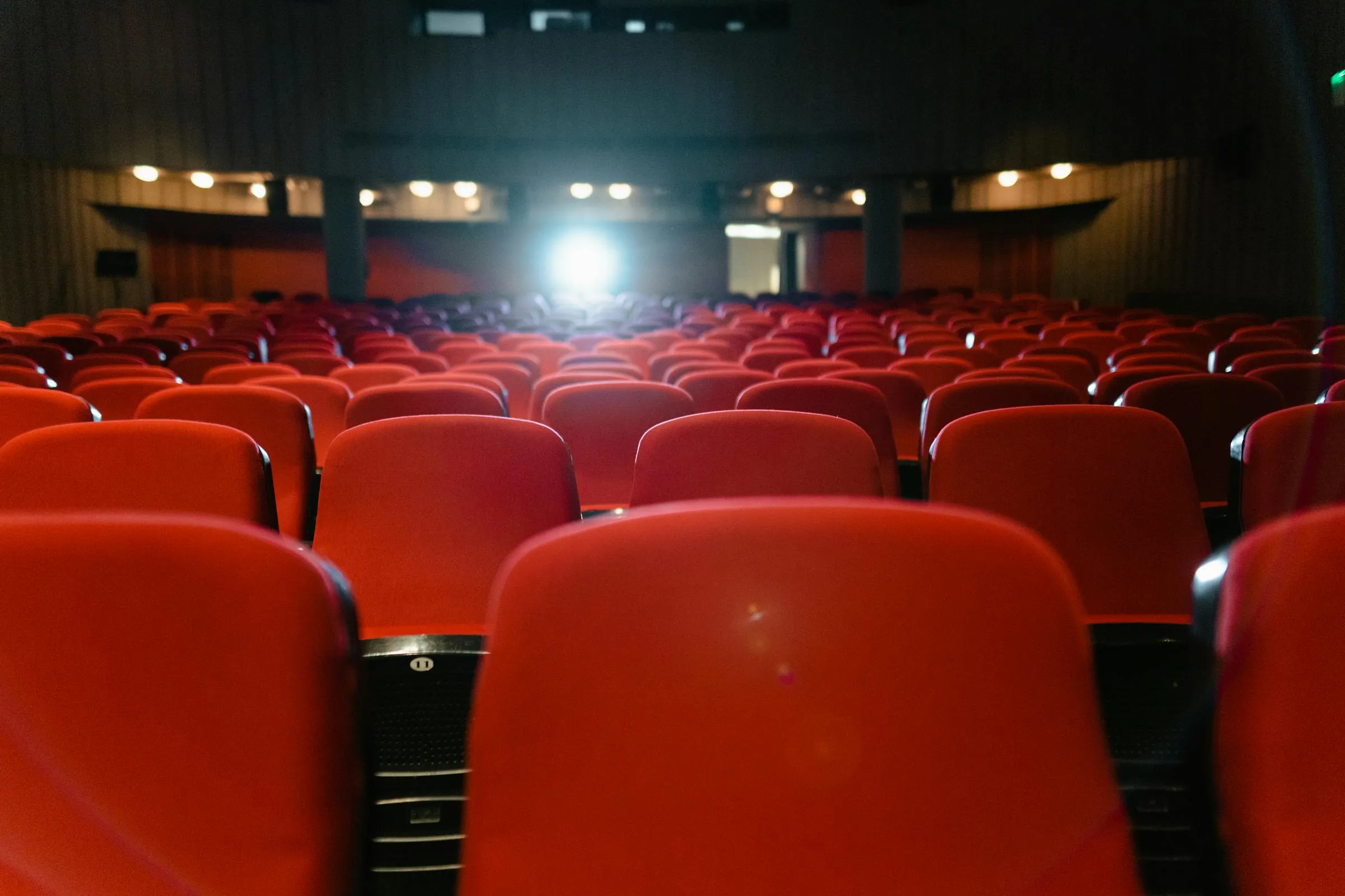 Empty cinema auditorium with rows of upholstered red seats facing the screen -- representative of the cinema seat recovery work we quote
