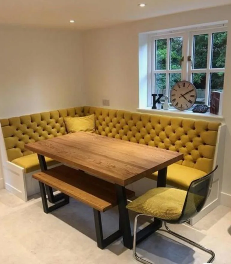 Deep-buttoned mustard banquette wrapped around a breakfast nook with timber table and matching cushion seat