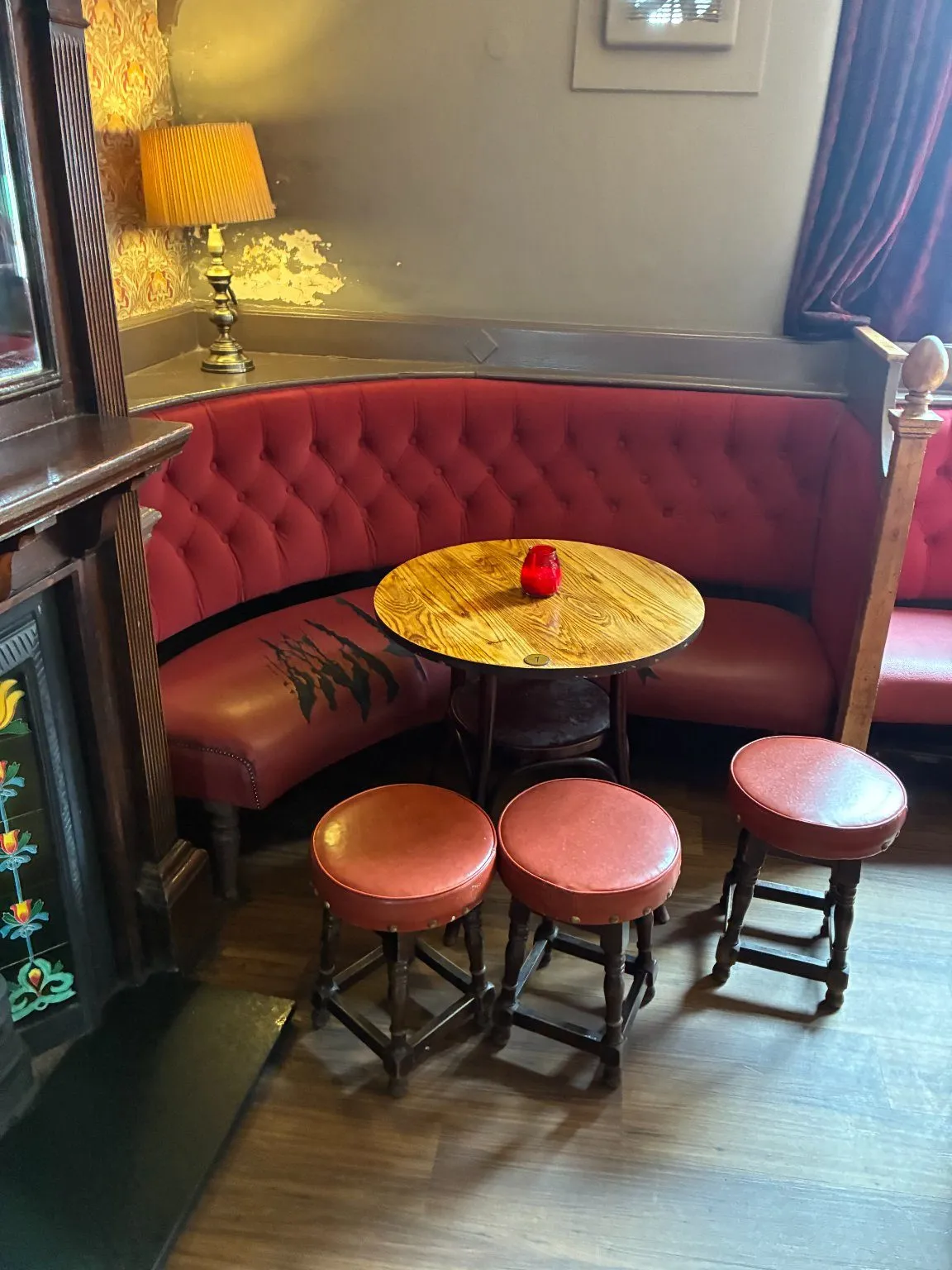 Curved red buttoned pub booth with round stools on a timber floor, before its seats were recovered