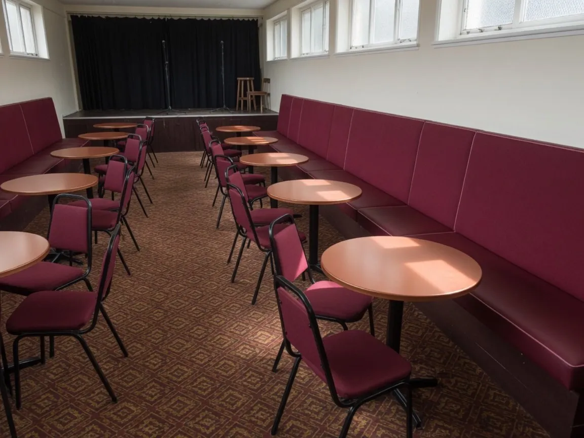 Club concert room with freshly recovered burgundy wall banquettes and matching chair pads in front of a small stage