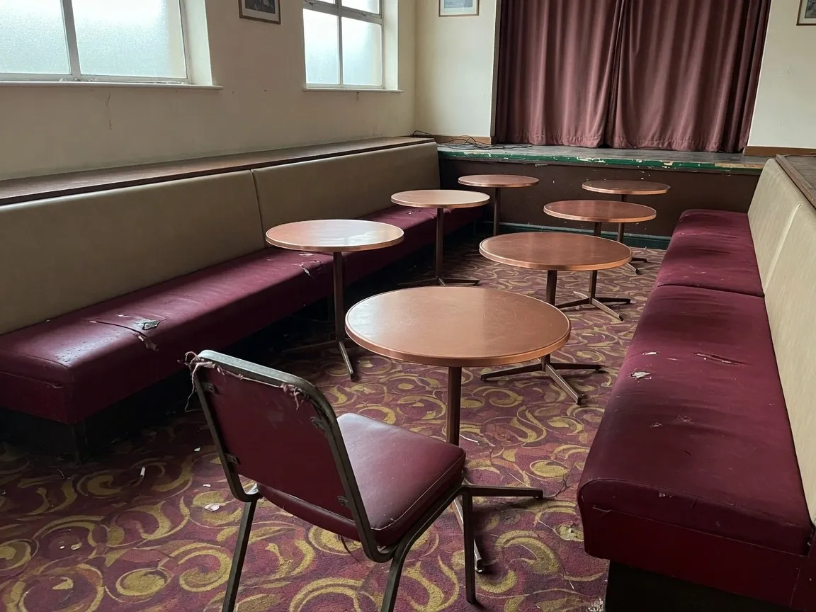 Club concert room with worn burgundy velour wall banquettes, copper-topped tables and a small stage