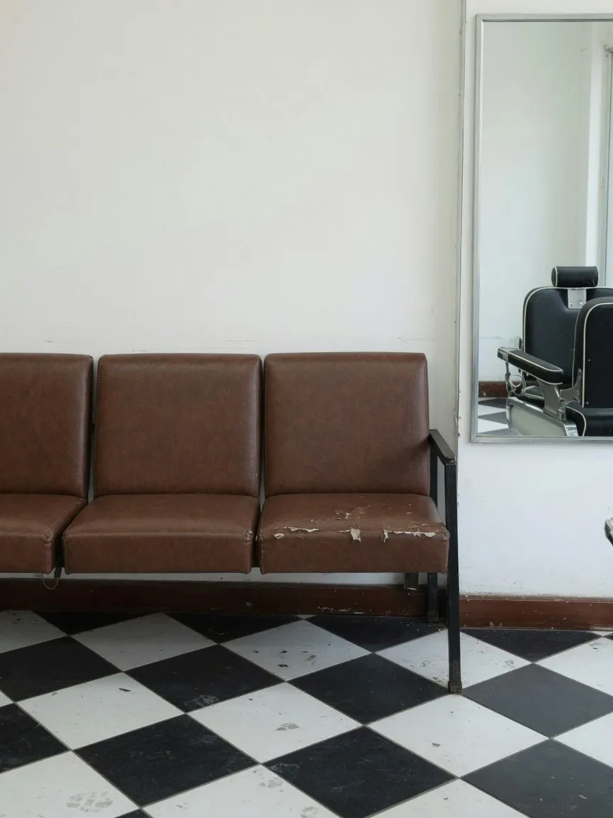 Barber shop waiting bench in scuffed brown faux leather on a black and white tiled floor